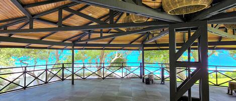 A covered outdoor area with a view of a blue body of water, metal beams, and a woven basket hanging from the ceiling.