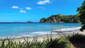 Une plage à l’eau d’un bleu cristallin, bordée d’un rivage sablonneux et d’une végétation luxuriante.