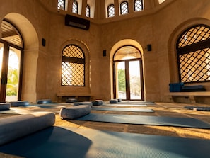 A yoga studio with mats and cushions arranged on the floor, large arched windows, and a view of greenery outside. - Reunion Wellness Resort & Retreats (Tempate)