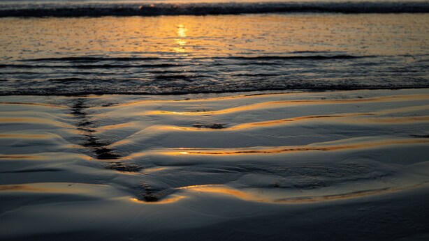 A beach with waves, a sunset, and a clear sky.
