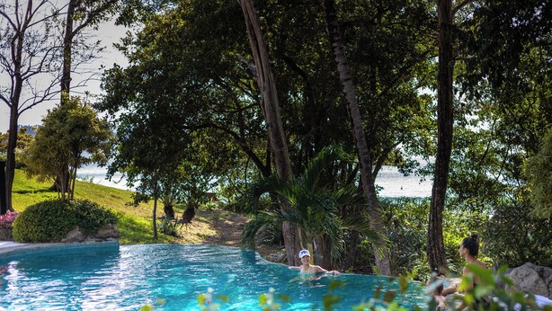 Une piscine entourée d’arbres, avec vue sur la mer.