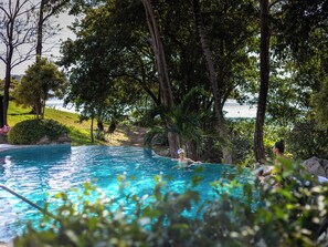 A swimming pool surrounded by trees and a view of the sea. - Reunion Wellness Resort & Retreats (Tempate)