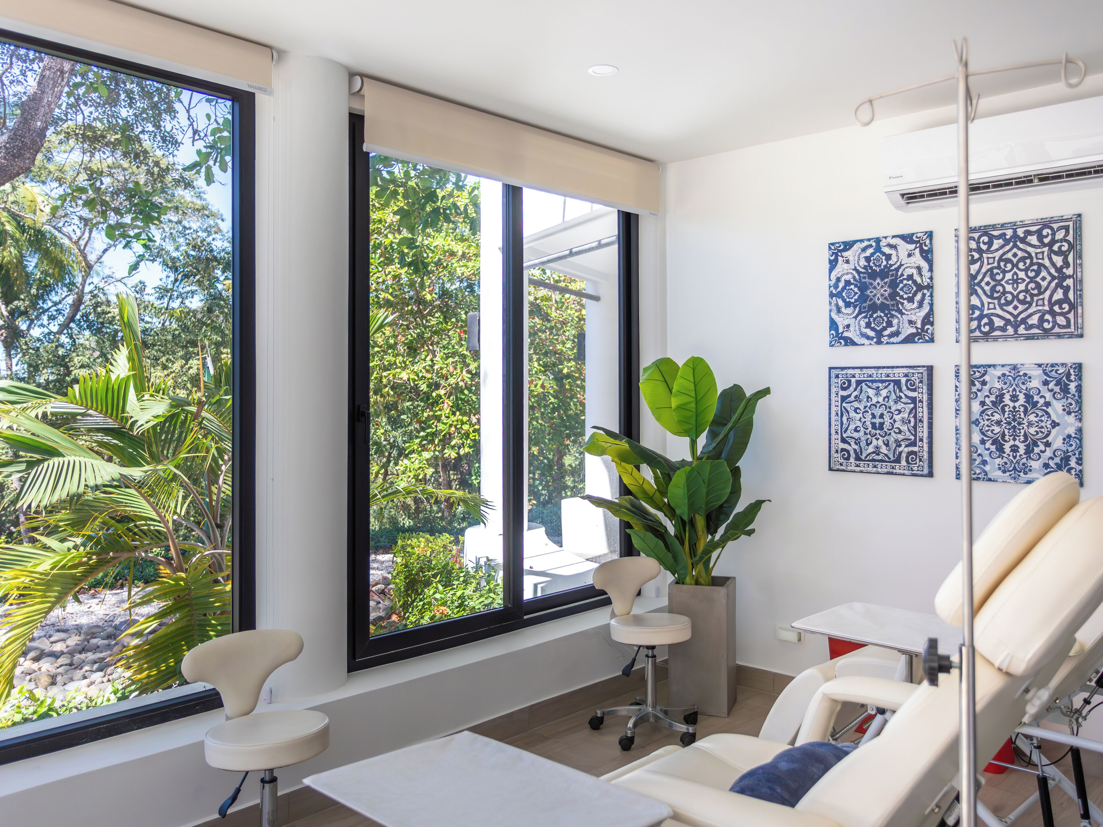 A modern room with large windows, a plant, a chair, a table, and a wall with blue and white tiles.