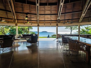 Un espace extérieur abrité, aménagé avec des sièges confortables et offrant une vue sur la mer, comprenant un bar et des fauteuils.