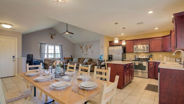 A spacious kitchen with wooden cabinets, a dining area with a wooden table set for four, and a living area with a sofa and a TV.
