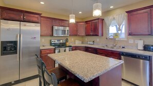 A kitchen with granite countertops, stainless steel appliances, wooden cabinets, and pendant lighting.