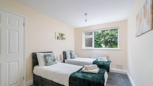 A bedroom with two beds, a window with a view of greenery, a radiator, and a door. - Redhill Retreat - Cozy 2 Bedroom Apartment (Redhill)