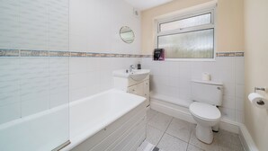 A bathroom with a bathtub, sink, toilet, and a window. - Redhill Retreat - Cozy 2 Bedroom Apartment (Redhill)