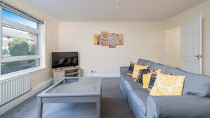 A living room with a grey sofa, a coffee table, a TV, and artwork on the wall. - Redhill Retreat - Cozy 2 Bedroom Apartment (Redhill)