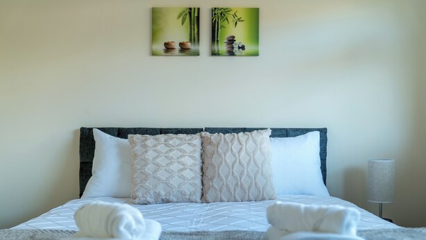 A neatly made bed with two pillows, a folded towel, and a lamp on a bedside table. - Redhill Retreat - Cozy 2 Bedroom Apartment (Redhill)