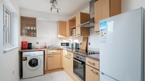 A modern kitchen with wooden cabinets, a built-in microwave, a stainless steel oven, and a white refrigerator. - Spacious 1 Bedroom Apartment w/ Parking in Crawley (Crawley)