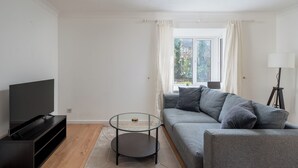 A modern living room with a flat-screen TV, a glass coffee table, a grey sofa, and a window with curtains. - Spacious 1 Bedroom Apartment w/ Parking in Crawley (Crawley)