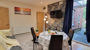 A dining area with a table set for four, a sofa, a TV, and a view of a brick building.