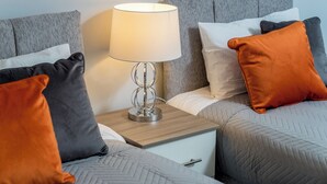 Una camera d'albergo con due letti, un comodino con una lampada e diversi cuscini.