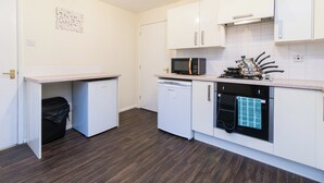 Una cocina compacta con armarios blancos, microondas, horno y lavavajillas.