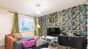Una sala de estar moderna con un sofá, una mesita redonda, un televisor y una mesa de comedor con sillas.