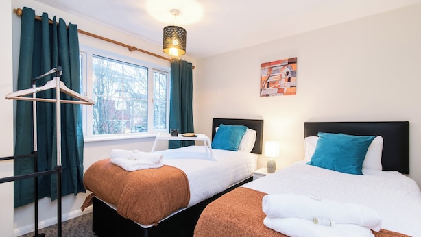 Habitación de hotel con dos camas, una ventana con cortinas, un perchero y un cuadro en la pared.
