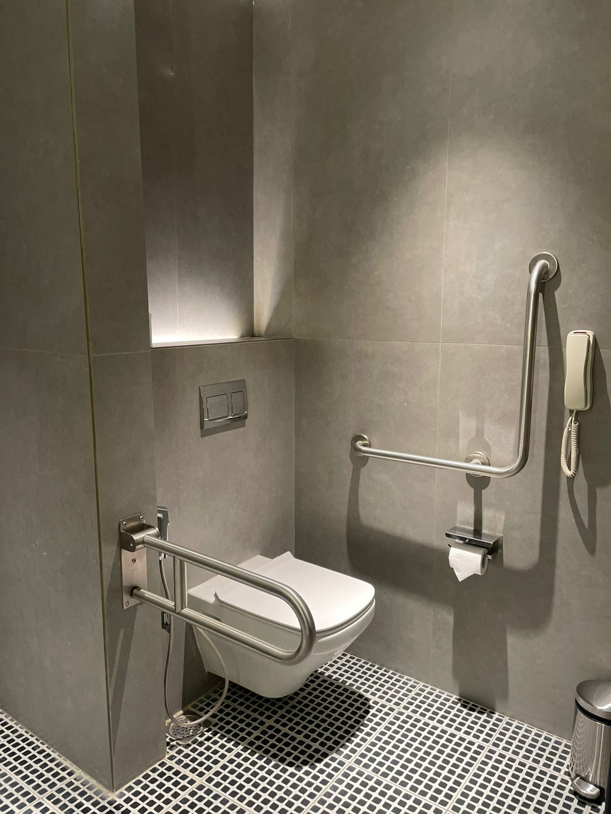 A modern bathroom with a toilet, grab bars, and a handrail.