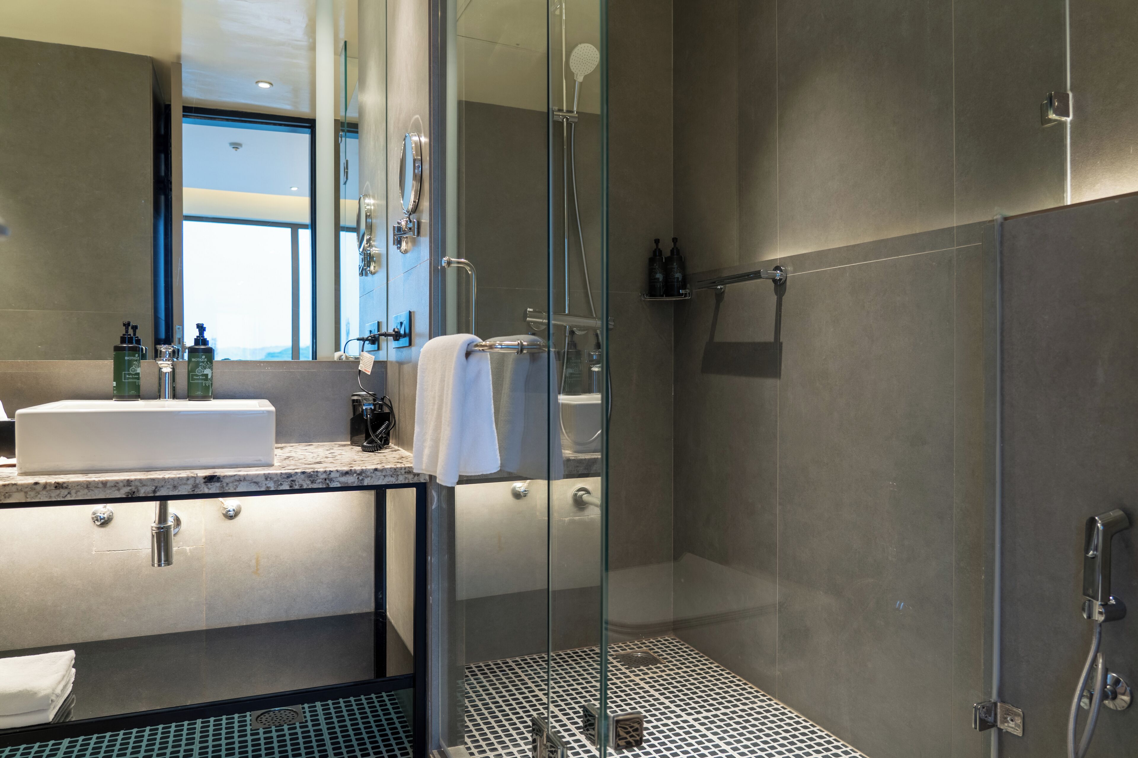 Un baño moderno con ducha de vidrio, un espejo grande y un lavamanos con toalla.