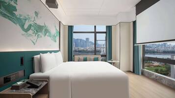 Una habitación de hotel moderna con una cama grande, un escritorio y vistas a un paisaje urbano a través de amplios ventanales.