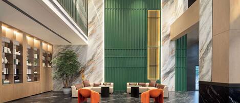 Eine Lobby mit Marmorboden, grünen Akustikpaneelen und zwei Sofas mit orangefarbenen Akzenten.
