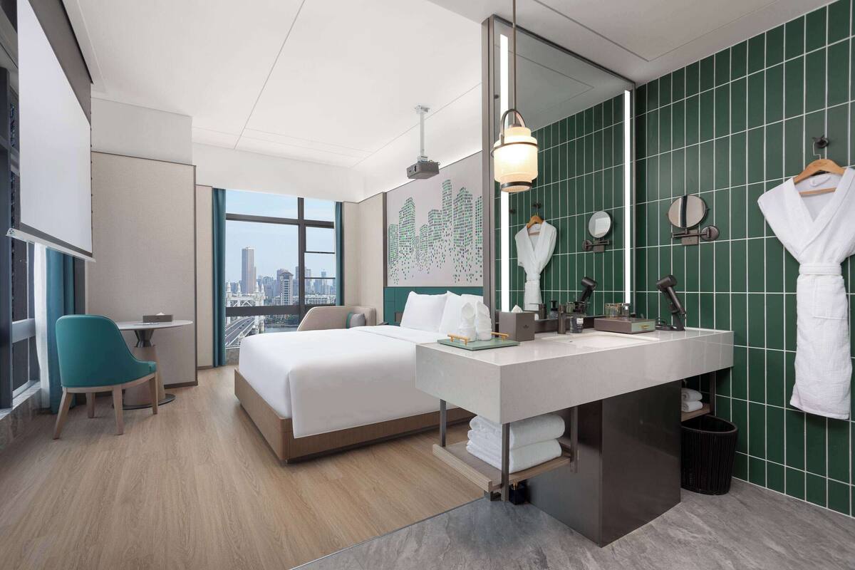 Une chambre d’hôtel moderne dotée d’un grand lit, d’un bureau et d’une salle de bain avec un miroir et un porte-serviettes.