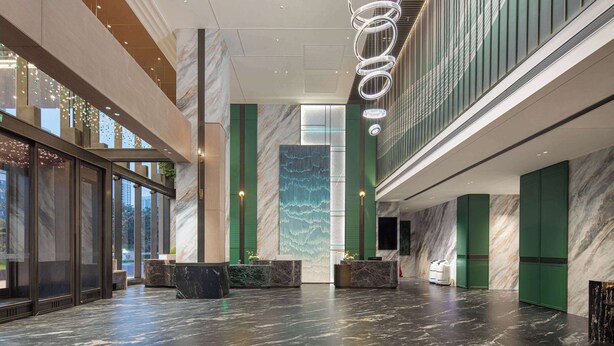 En rymlig entréhall med marmorgolv, en stor, vertikal vatteninstallation och modern belysning.