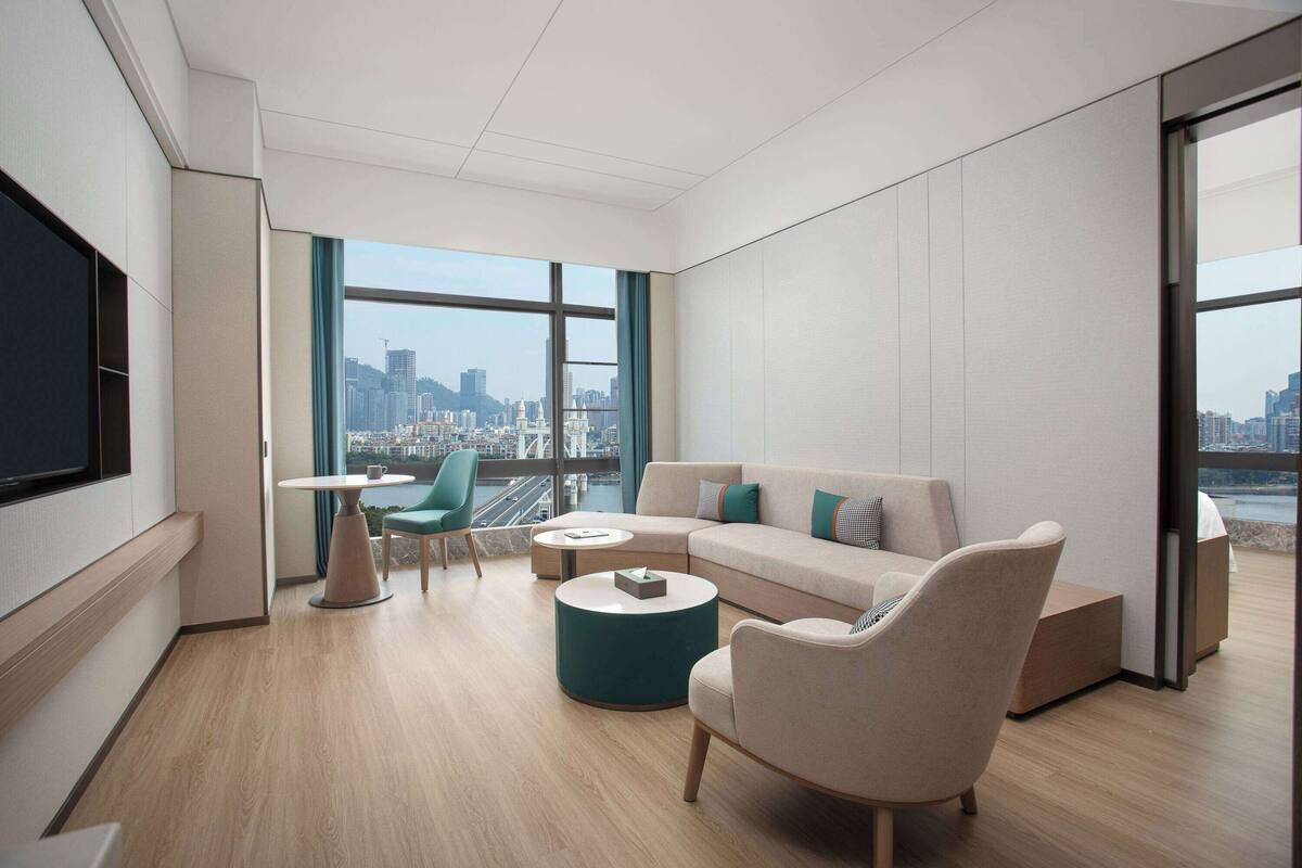 Un salon moderne avec vue sur la ville, comprenant un canapé, deux fauteuils, une table basse et un téléviseur.