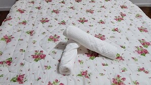 A bed with a floral bedspread and a rolled towel. - SUA CASA NO RIO-COPACABANA 3 QTS (Rio de Janeiro)