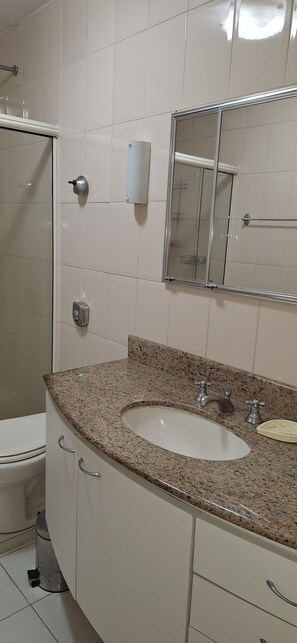 Une salle de bain avec un lavabo surmonté d’un plan de travail en granit, un miroir, des toilettes et un espace douche.