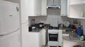 A compact kitchen with white cabinets, a stove, a sink, and a refrigerator. - SUA CASA NO RIO-COPACABANA 3 QTS (Rio de Janeiro)