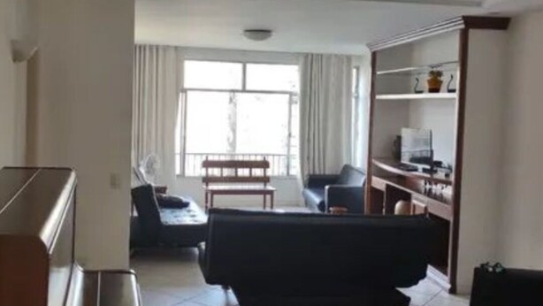 A spacious living room with a black sofa, a wooden coffee table, and a dining area with a bench. - SUA CASA NO RIO-COPACABANA 3 QTS (Rio de Janeiro)