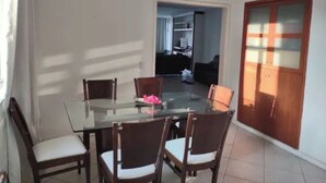 A dining area with a glass table and wooden chairs, a ceiling fan, and a view into a living space. - SUA CASA NO RIO-COPACABANA 3 QTS (Rio de Janeiro)