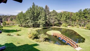 Ein Golfplatz mit Teich, einer Holzbrücke und dichtem Wald im Hintergrund.