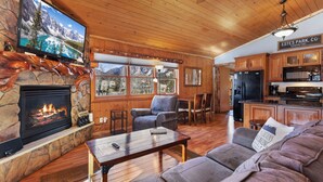 Ein gemütliches Blockhaus-Interieur mit Kamin aus Stein, einem an der Wand befestigten Fernseher, Holzmöbeln und einer Küchenzeile.