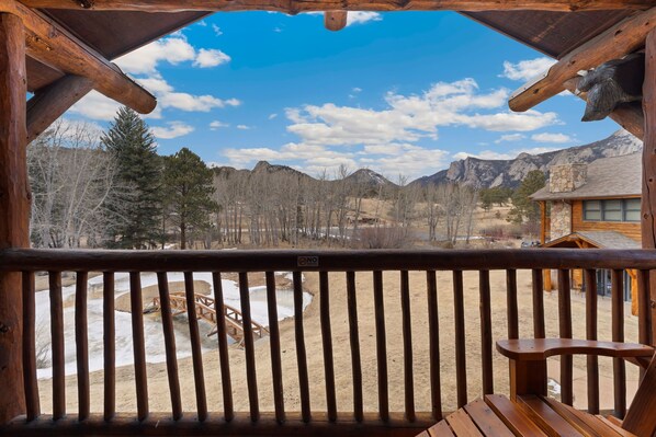 Eine Holzterrasse mit Blick auf eine gebirgige Landschaft, ein Steinhaus und ein Holzstuhl.