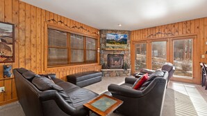 Una sala de estar acogedora con sofás de cuero, chimenea de piedra, paneles de madera y ventanas amplias con persianas.