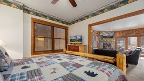 Un dormitorio con una cama grande, cabecera de madera, colcha, televisión, chimenea y vistas al exterior.