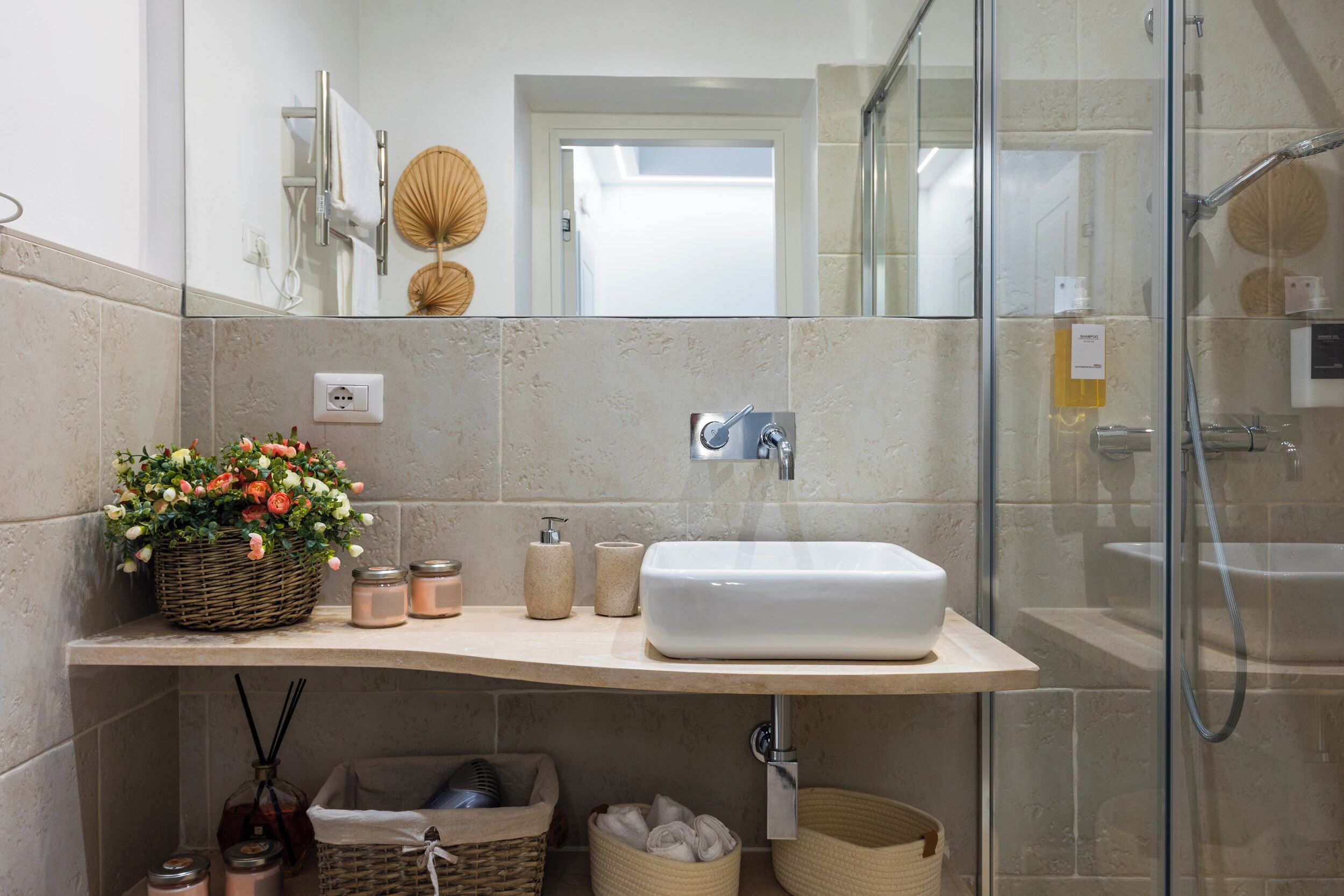 A modern bathroom with a large mirror, a white sink, and a glass-enclosed shower.