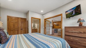 A bedroom with a bed, wooden wardrobe, and a TV on the wall.