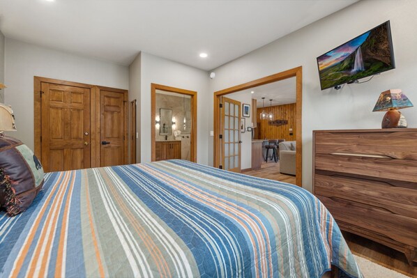 A bedroom with a bed, wooden wardrobe, and a TV on the wall.