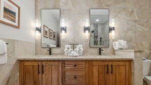 A bathroom with marble walls, wooden cabinets, and two large mirrors.