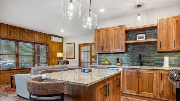 A modern kitchen with wooden cabinets, a granite island, and pendant lighting.