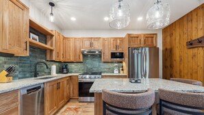 A kitchen with wooden cabinets, a stainless steel dishwasher, a double oven, and a refrigerator. There are two bar stools and a small island with a sink.