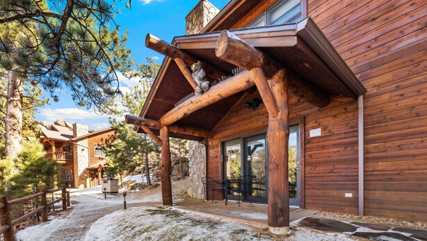 Une cabane en bois avec une cheminée en pierre, une véranda et un sol recouvert de neige.