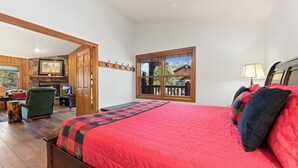 A bedroom with a large bed, a wooden chair, a fireplace, and a window with a view of a house.