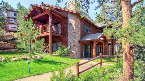 A log cabin with a stone chimney, a balcony, and a wooden deck.