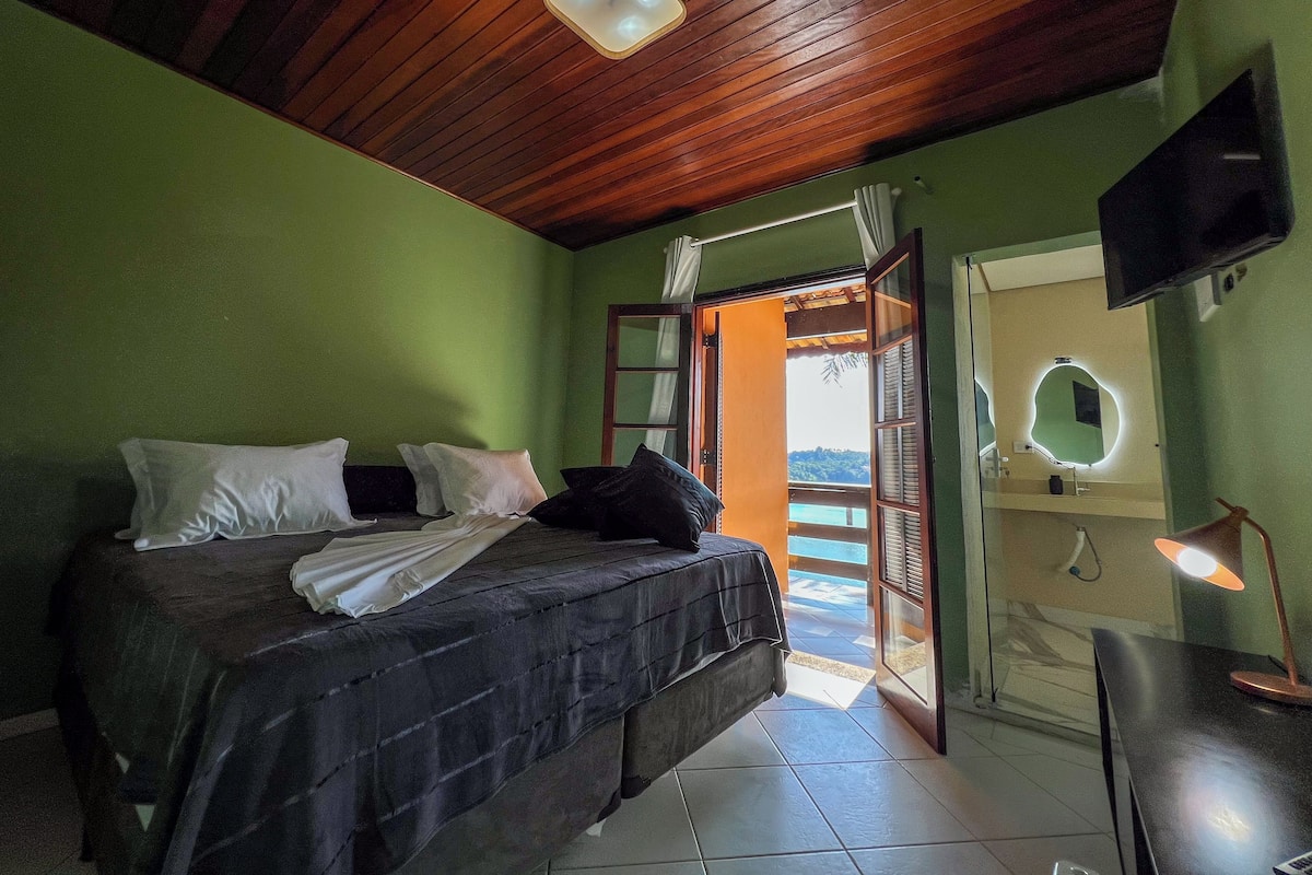 Un dormitorio con cama, almohadas, un escritorio con lámpara, televisión y vistas a un balcón con piscina.
