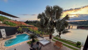 A rooftop pool area with lounge chairs, a table, and a view of a river and bridge. - Pousada Recanto de Igaratá (Igarata)
