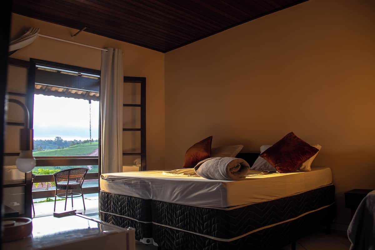 Un dormitorio con cama, almohadas, una silla y ventana con vistas al exterior.